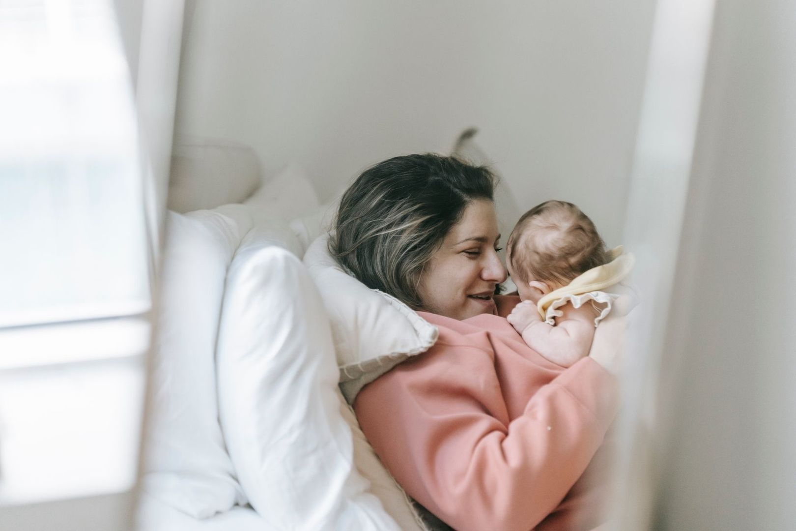 Mamma håller en bebis nära sig i en ljus sängmiljö